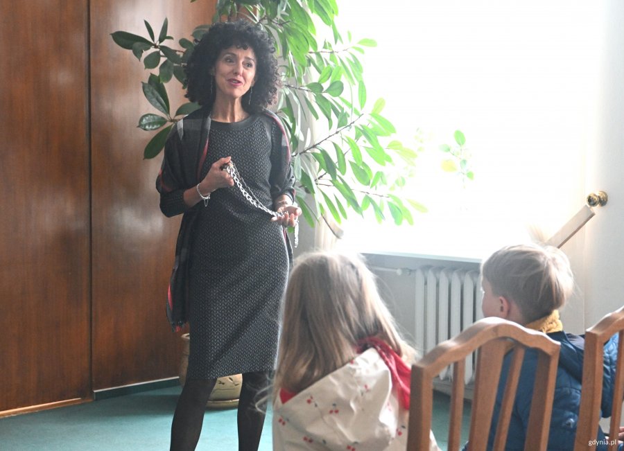 Kobieta w sukience pokazuje dzieciom łańcuch z orłem