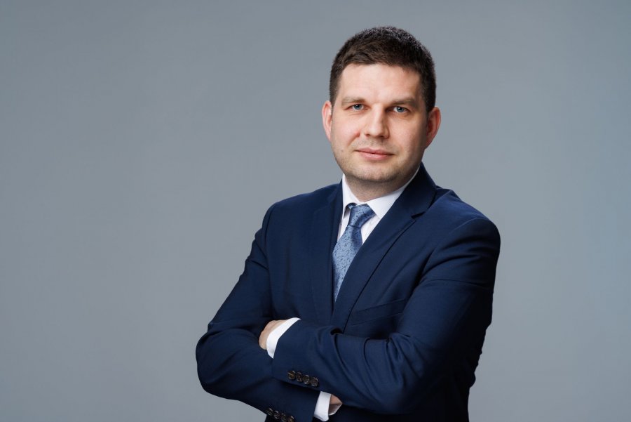 Zdjęcie portertowe: Maciej Zielonka, Wiceprezydent Miasta Gdyni, w garniturze, białej koszuli i krawacie, na szarym tle. 