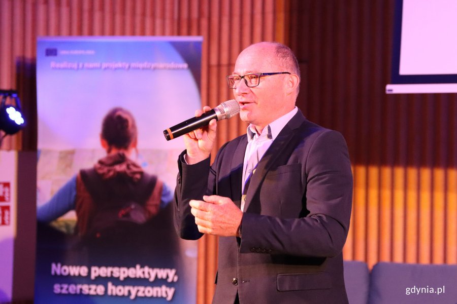 Mężczyzna przemawiajacy przed widownią z mikrofonem w ręku