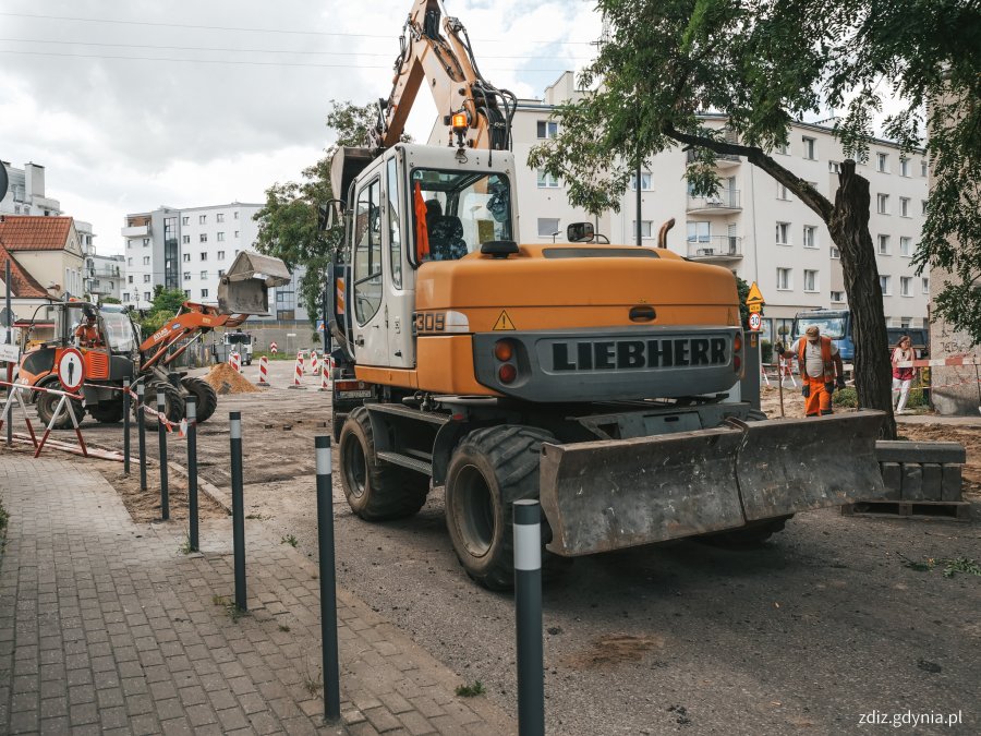 na pierwszym planie pojazd wykonujący roboty drogowe, w tle trwa wymiana nawierzchni na skrzyżowaniu, widoczne oznakowanie