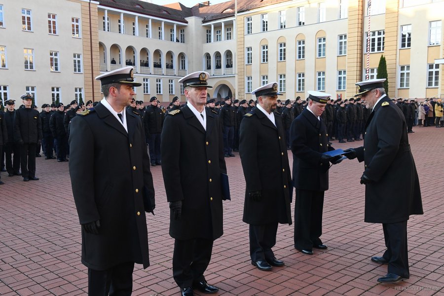 Oficer Marynarki Wojennej wręcza nominacje czterem żołnierzom Marynarki Wojennej w mundurach.