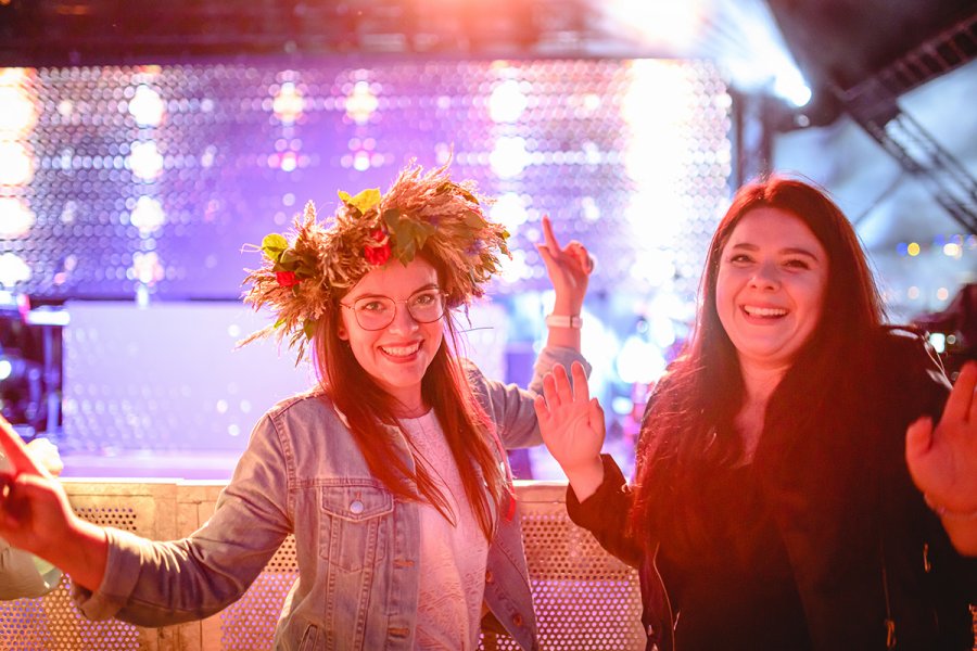 Dwie młode kobiety bawią się podczas koncertu na plaży. Jedna ma wianek na głowie.