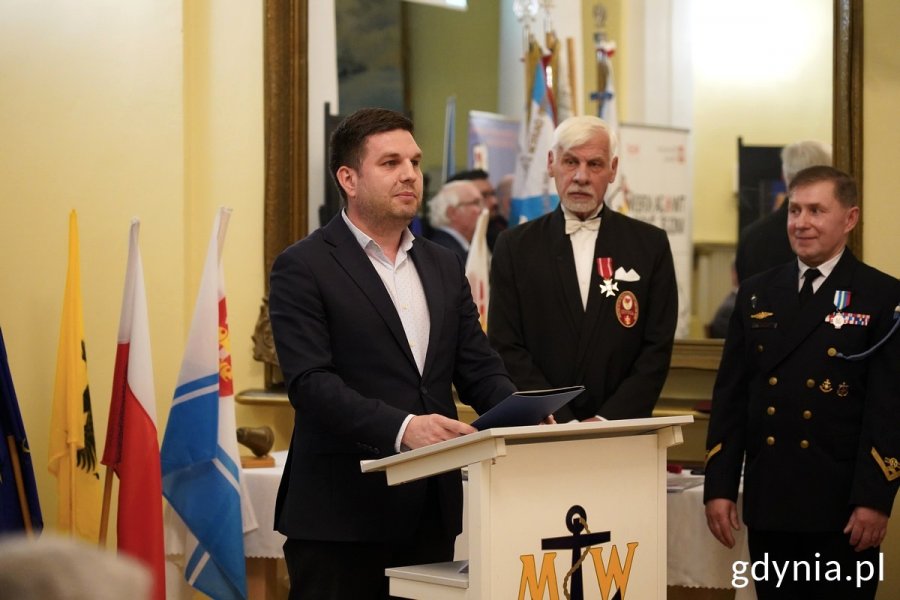 Przy mównicy wiceprezydent Gdyni Maciej Zielonka, obok stoją prezes klubu Paweł Szczepanik i sekretarz klubu Michał Bijo 