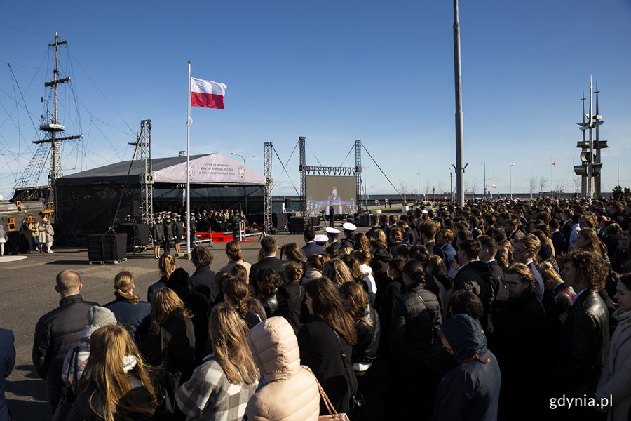 Trybuna honorowa na placu, przed nią tłum studentów.