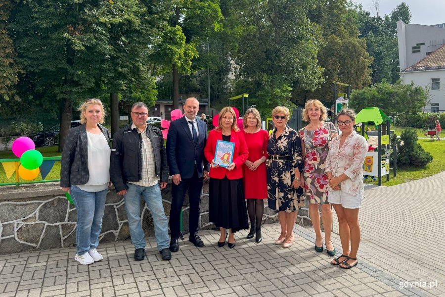 Grupa uśmiechnietych ludzi ustawiona do zdjęcia, w tle plac zabaw