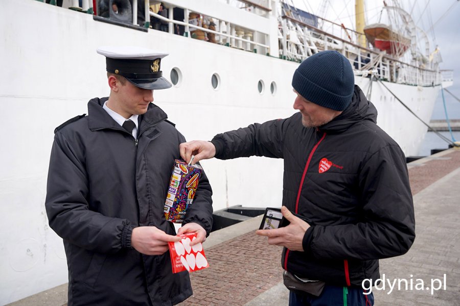 Wolontariusz WOŚP w mundurze marynarskim zbiera pieniądze do puszki.