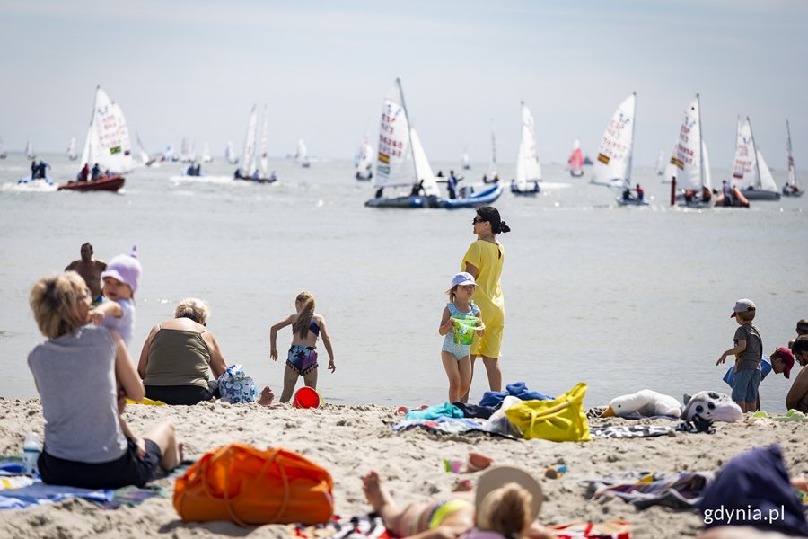Ludzie na plaży, w tle żaglówki na morzu.