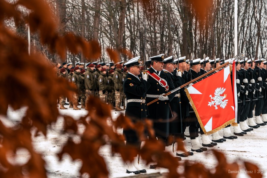 Marynarze Marynarki Wojennej stoją ze sztandarem na cmentarzu.