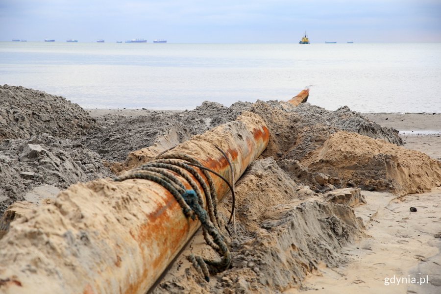 Spychacz jeździ po plaży wychodzaca z morza.