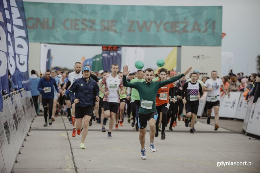 Biegacze na starcie biegu, na pierwszym planie mężczyzna machający rękoma w zielonej bluzie. 