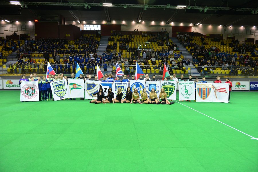 Zawody sportowe na hali. Zdjęcie grupowe z udziałem cheerleaderek oraz herbów i flag klubów. W tle widoczne trybuny. 