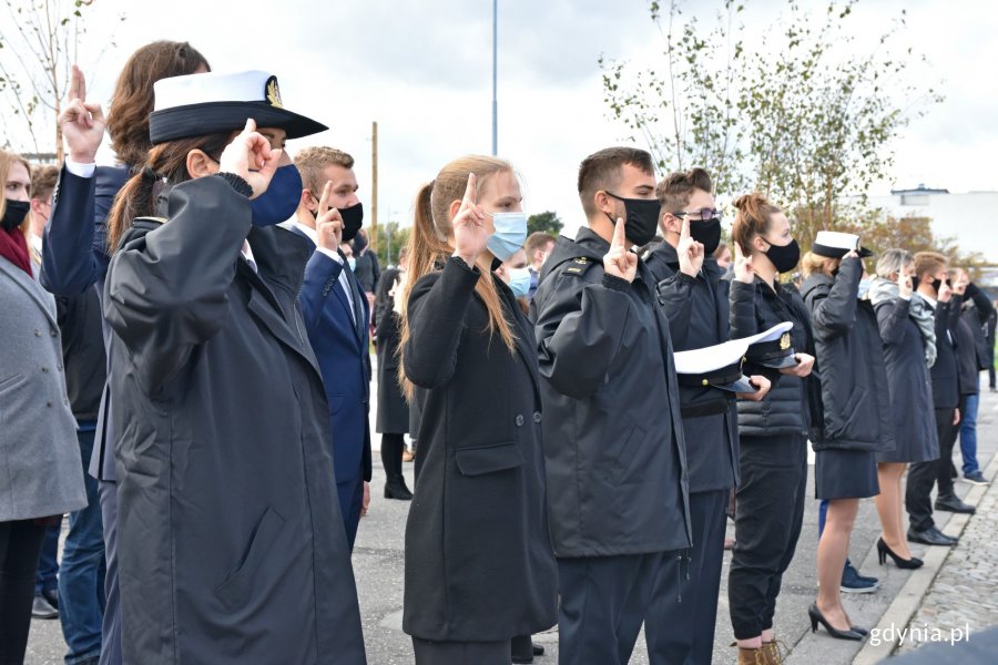 Studenci Uniwersytetu Morskiego podczas ślubowania - salutują lub mają podniesione dłonie. Są ubrani w ciemne kurtki lub mundury // fot. Magdalena Czernek