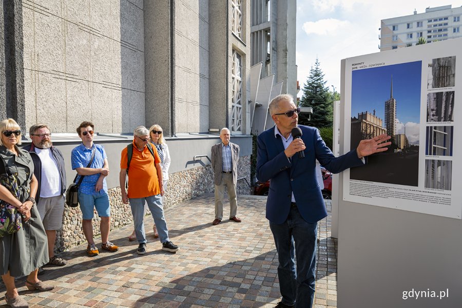 Ludzie oglądają wystawę przed kościołem, o której opowiada jeden mężczyzna.