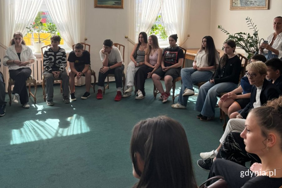 Przedstawiciele Młodzieżowej Rady Miasta Gdyni oraz młodzieży z Gruzji. Kilkanaście osób w różnym wieku, kobiety i mężczyźni. Siedzą w okręgu na fotelach, w sali wizytowej podczas spotkania i rozmowy. 