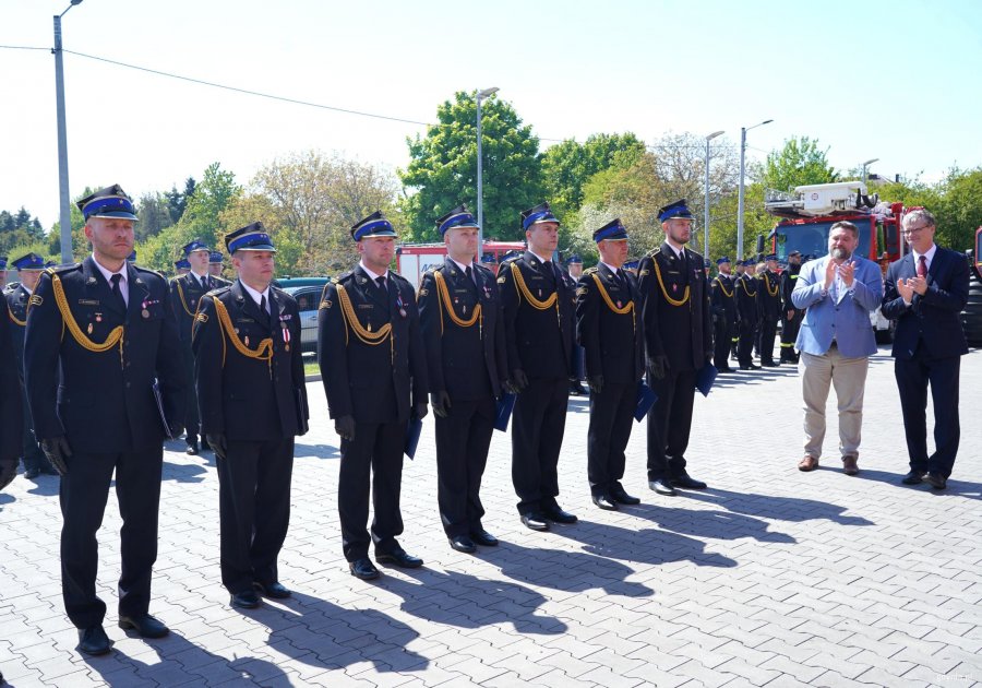 Strażacy w mundurach i dw&oacute;ch mężczyzn bije im brawo