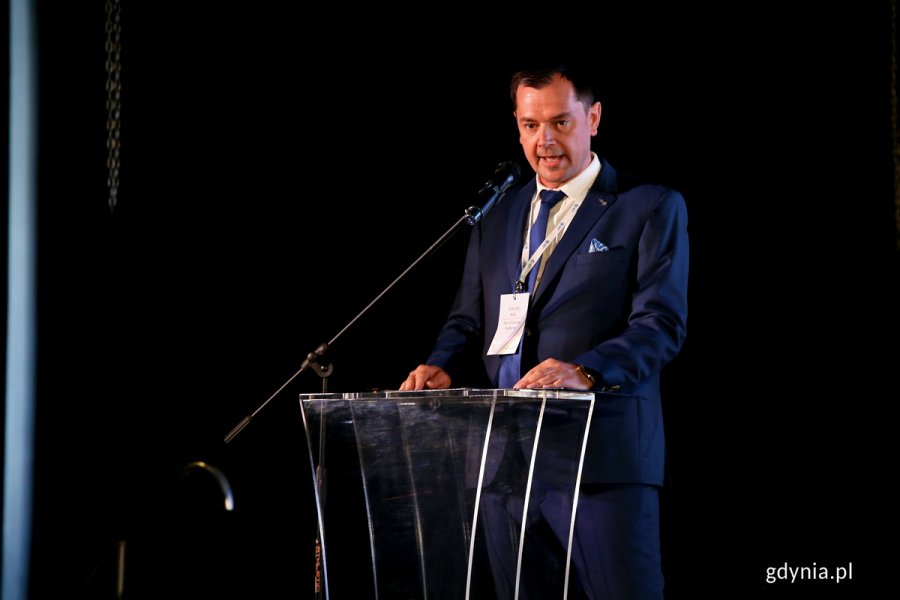 Męzczyzna przemawia na mównicy w sali konferencyjnej.