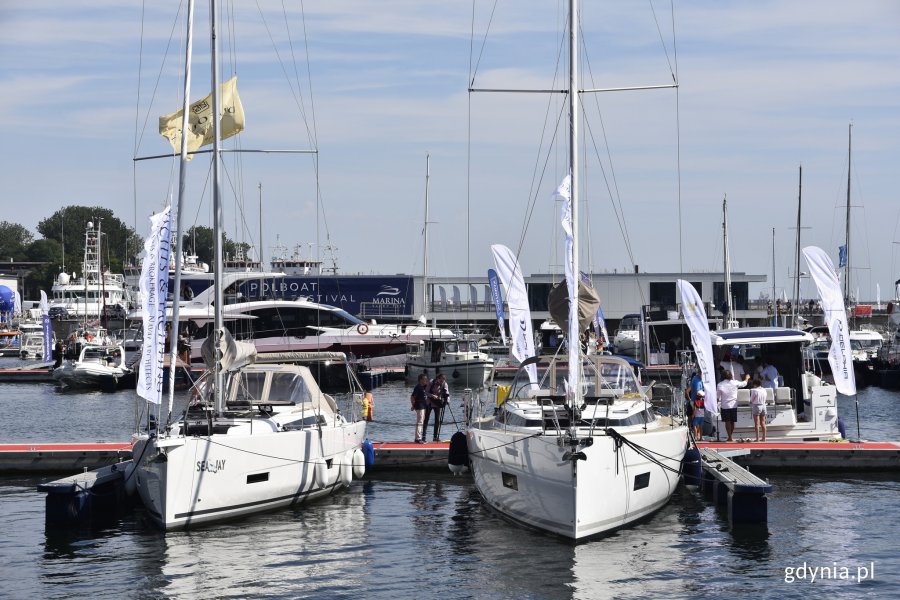 Dwa białe jachty są zacumowane przy kei w Marina Yacht Parku w Gdyni. Na kei ludzie oglądający łodzie. W tle inne jachty // fot. Magdalena Czernek