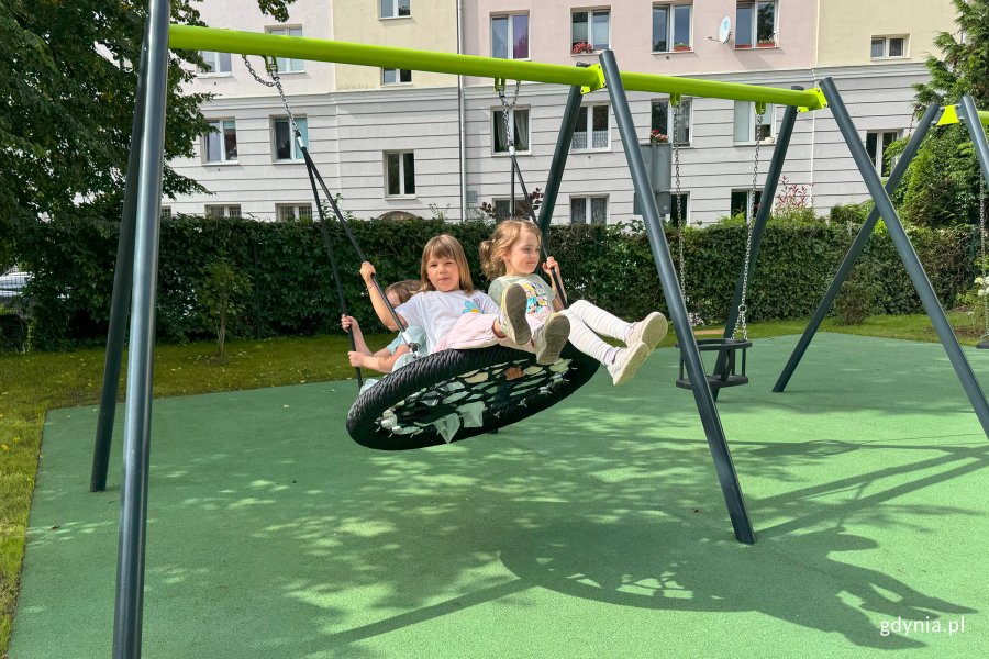 Chłopiec na placu zabaw, na trampolinie, w tle na schodach przed budynkiem ludzie świętujący uroczystość