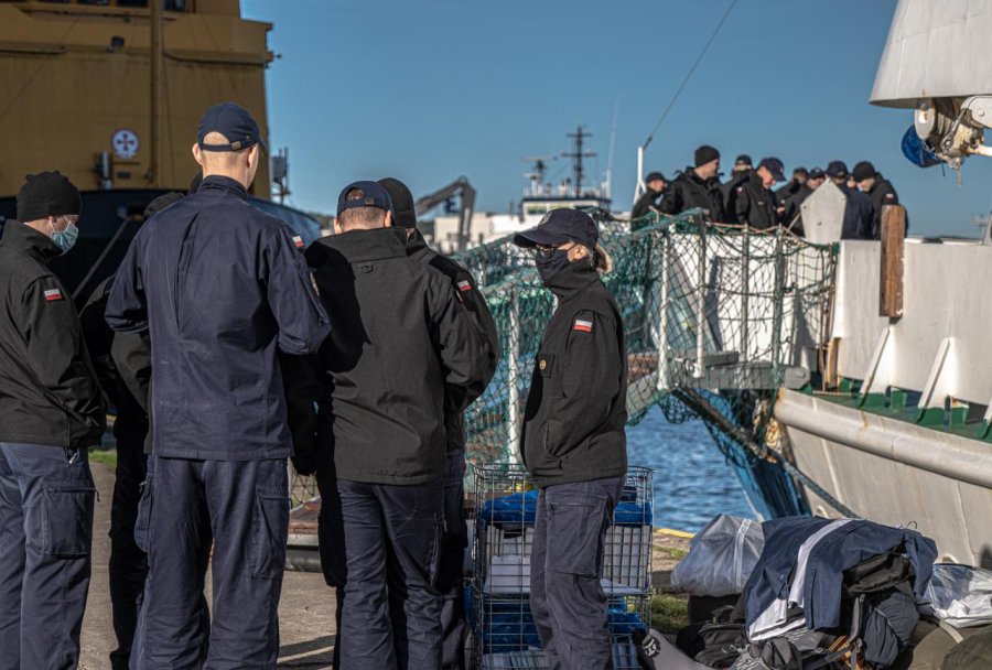 Podchorążowie Akademii Marynarki Wojennej w Gdyni przed i na pokładzie statku "Horyzont II". Są ubrani w granatowe spodnie i czarne kurtki z przyszytymi do rękawów biało-czerwonymi flagami. Na głowach mają czapki z daszkiem, a na twarzach maseczki // fot. Piotr Lewandowski / Uniwersytet Morski w Gdyni