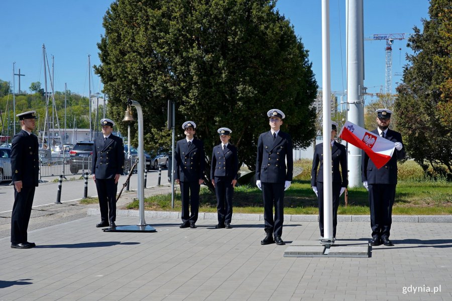 Poczet flagowy i przedstawiciele student&oacute;w podczas podniesienia bandery na maszt na uroczystym apelu z okazji otwarcia sezonu żeglarskiego w Ośrodku Żeglarstwa i Sport&oacute;w Wodnych Uniwersytetu Morskiego