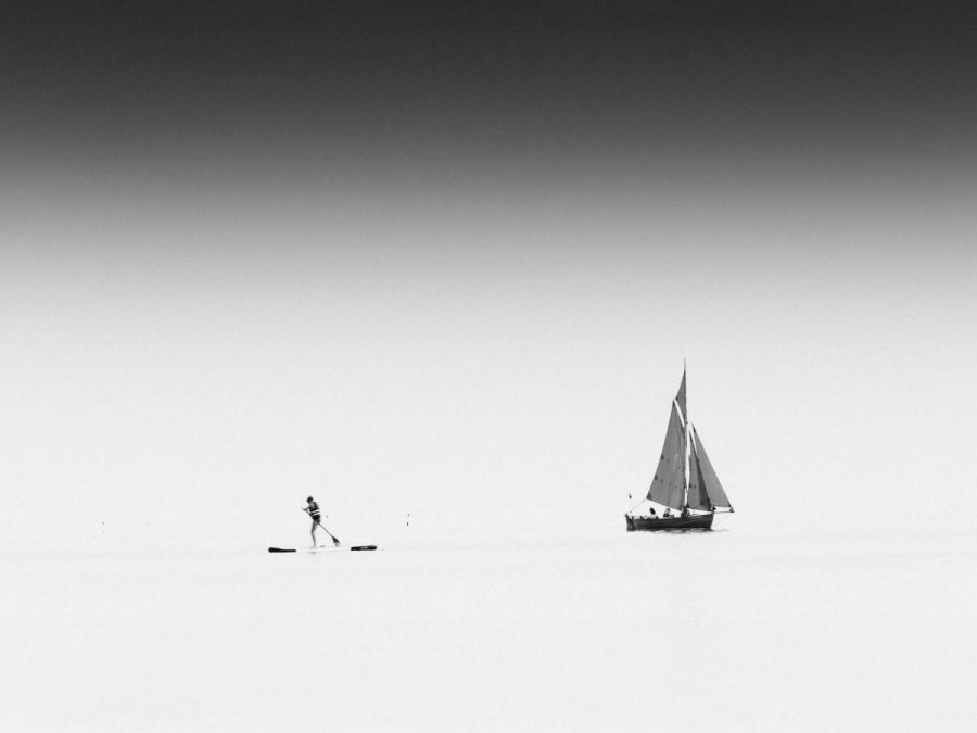 Czarno-białe zdjęcie przedstawiające żaglówkę i łódź typu SUP na powierzchni morza
