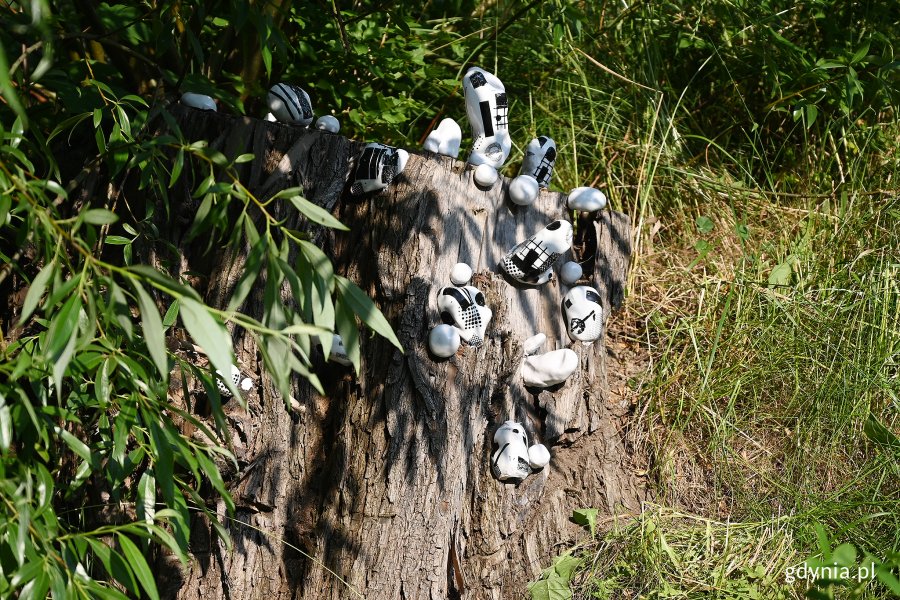 Instalacja autorstwa Agnieszki Jewasińskiej. Na pieńsku drzewa umieszczone są białe akcesoria sportowe - piłki, rękawice z wymalowanymi na czarno wzorami // fot. Michał Puszczewicz