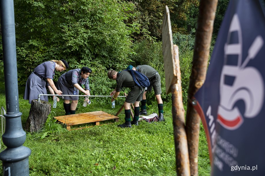 Harcerki i harcerze napełniają butelki wodą z kranu.