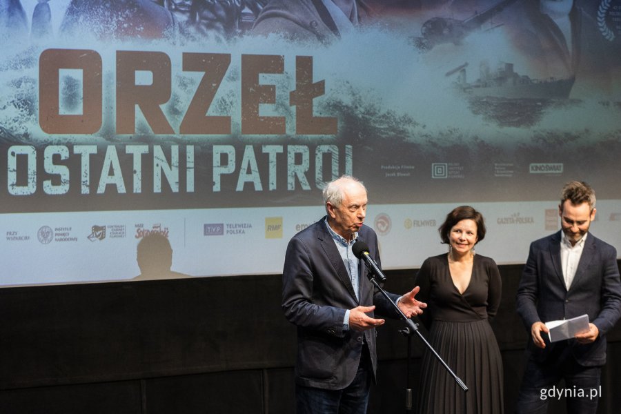 Gdyńska premiera filmu „Orzeł. Ostatni patrol”. W sali kinowej Gdyńskiego Centrum Filmowego przy mikrofonie stoi Leszek Kopeć i prowadzący uroczystość