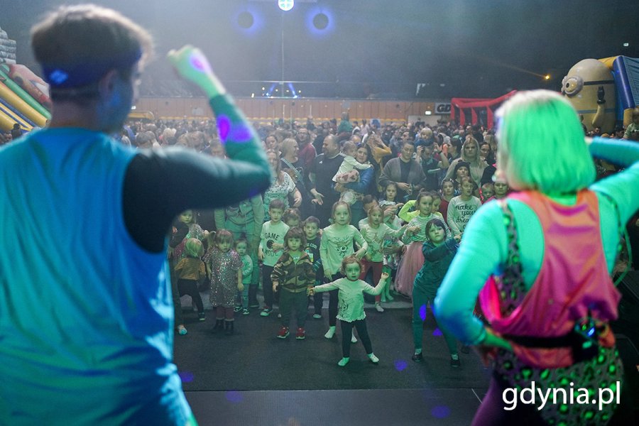 Dzieci tańczą pod sceną, na której tańczą animatorzy.
