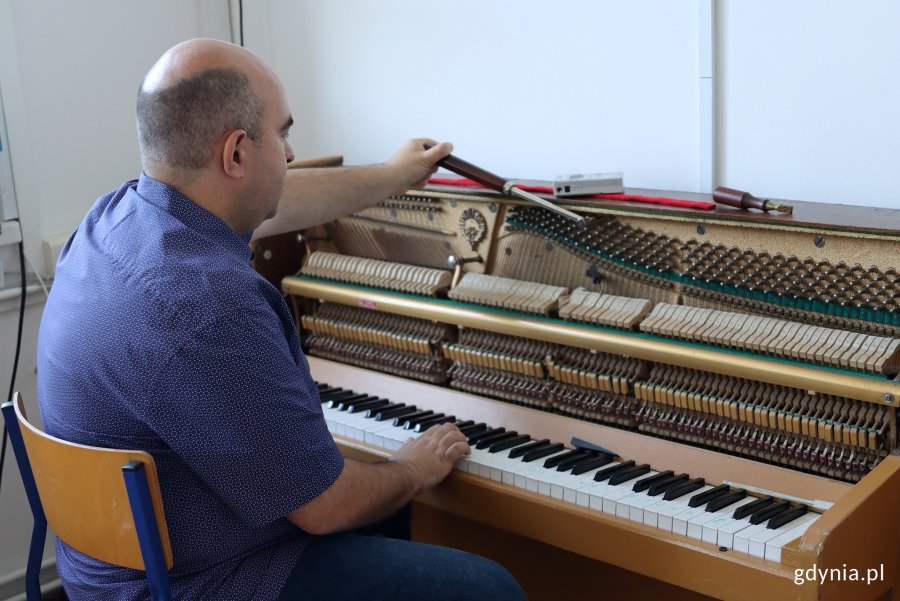 Mężczyzna siedzący na krześle, twarzą do pianina, w rękach trzyma narzędzia do strojenia pianina