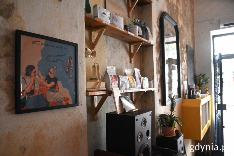 Wnętrze kawiarni „Kosmos”: półki z kawą i sierpniowa grafika Pawła Smardzewskiego