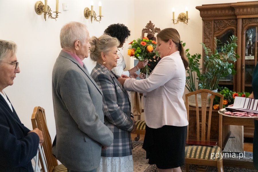 Prezydent wręcza medal kobiecie w marynarce w kratę, obok jej mąż