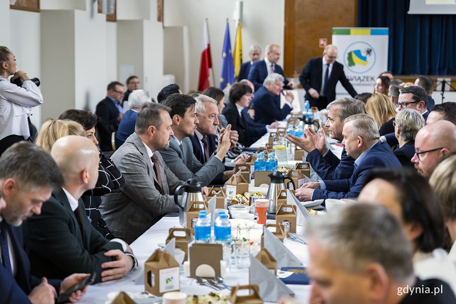 Ludzie zgromadzeni na sali siedzą za stołami.