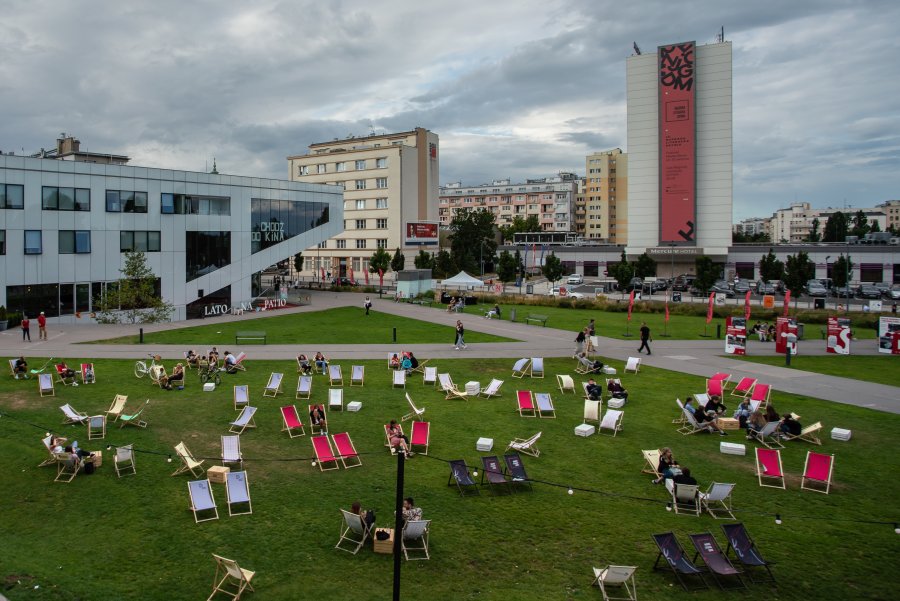 Różnokolorowe leżaki są rozstawione na trawie na placu Grunwaldzkim. W tle budynek Gdyńskiego Centrum Filmowego i hotelu Mercure, na którym jest rozwieszony czerwono-czarny baner Nagrody Literackiej GDYNIA // fot. Anna Rezulak