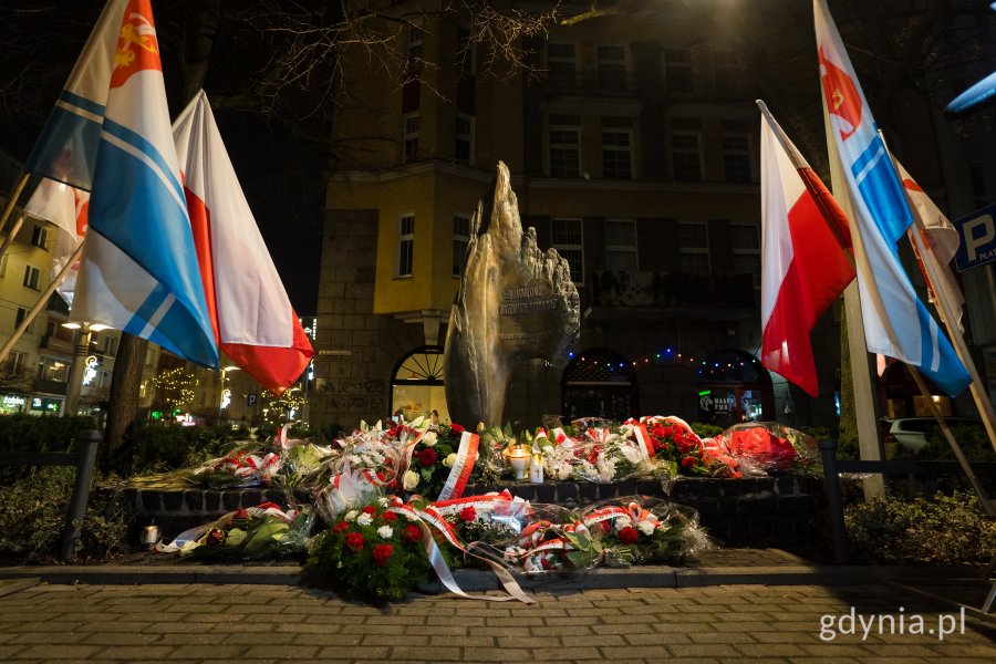Kwiaty i znicze pod pomnikiem Ofiar Terroru Komunistycznego w otoczeniu flag Polski i Gdyni