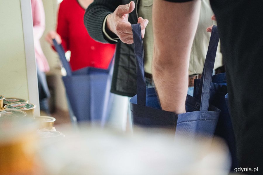Pakowanie wielkanocnych paczek dla potrzebujących, które odbyło się w Centrum Aktywności Seniora. Na zdjęciu widać ręce wolontariuszy, którzy trzymają siatki. Inni wkładają do nich produkty // fot. Kamil Złoch