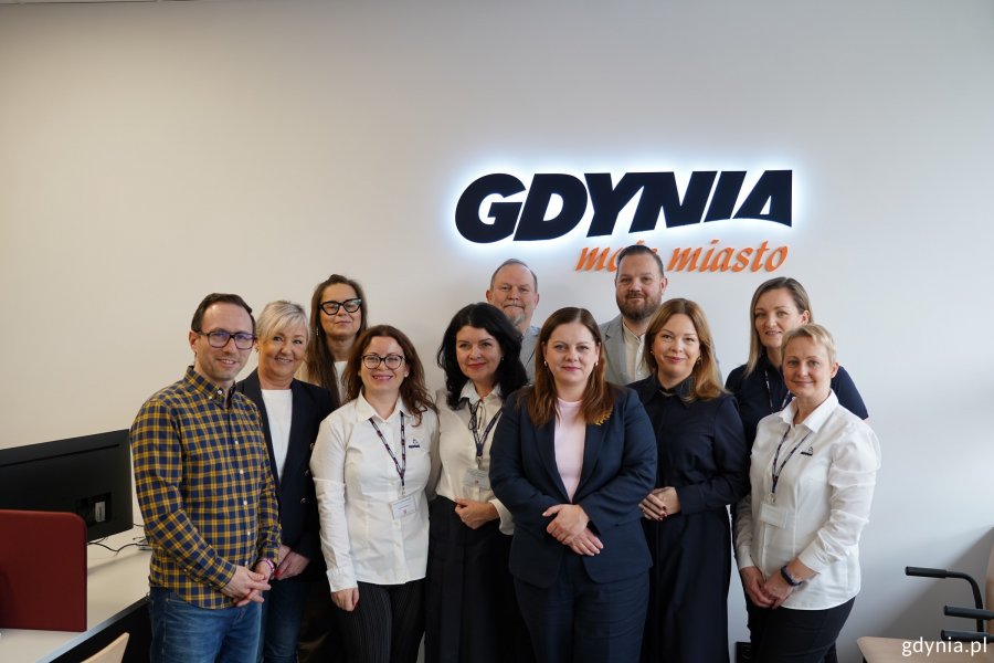 Obsługa punktu przy ul. Unruga 39 w towarzystwie prezydent Aleksandry Kosiorek, wiceprezydentki Oktawii Gorzeńskiej, radnego miasta Łukasza Strzałkowskiego oraz radnych dzielnicy Obłuże: Macieja Dobbka, Izabeli Procelli-Szynwelskiej i Marka Urbaniaka na tle napisu: Gdynia moje miasto