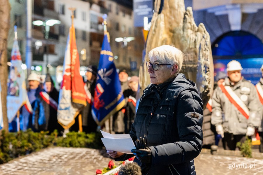 na zdjęciu kobieta czytająca z kartki i odświętnie ubramne osoby