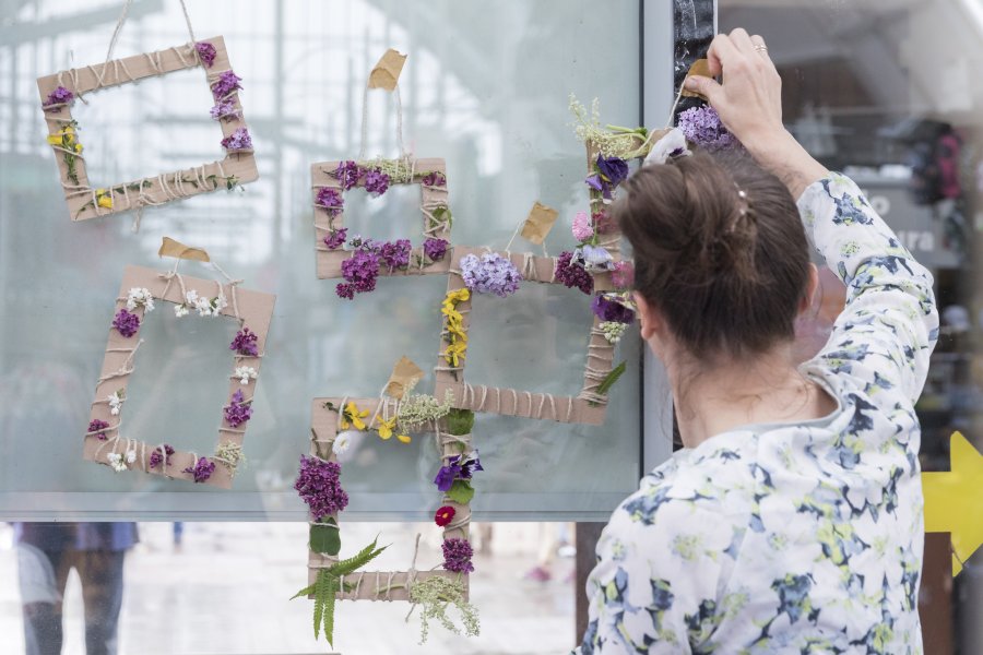 Ramki kwiatowe stworzone przez uczestników zabaw plastyczno-sensorycznych, które odbyły się w ramach "Dnia Kreatywnego" w Miejskich Halach Targowych. Kobieta przyczepia prace do szklanek tablicy // fot. Sandra Szmigiel