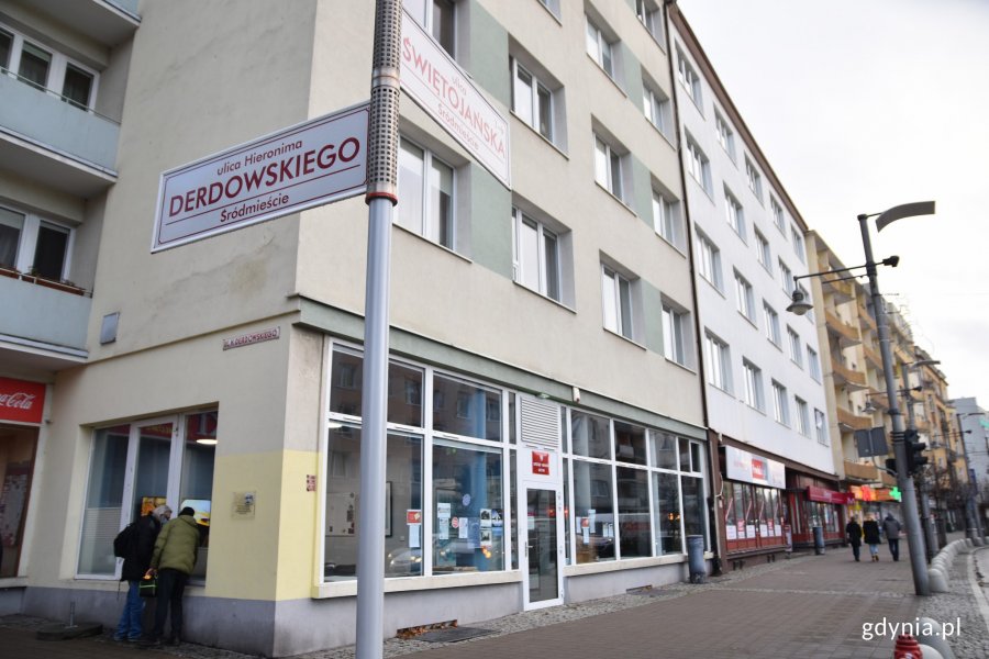 Tablica pamiątkowa została zamontowana na bocznej fasadzie kamienicy na rogu ulic Świętojańskiej i Derdowskiego. Na pierwszym planie drogowskaz z nazwami ulic. W tle budynek oraz mężczyźni montujący tablicę // fot. Sławomir Okoń