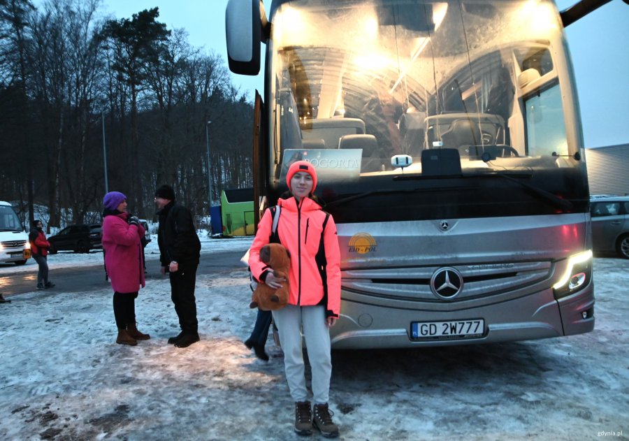 Nastolatka w pomarańczowej kurtce przed autokarem