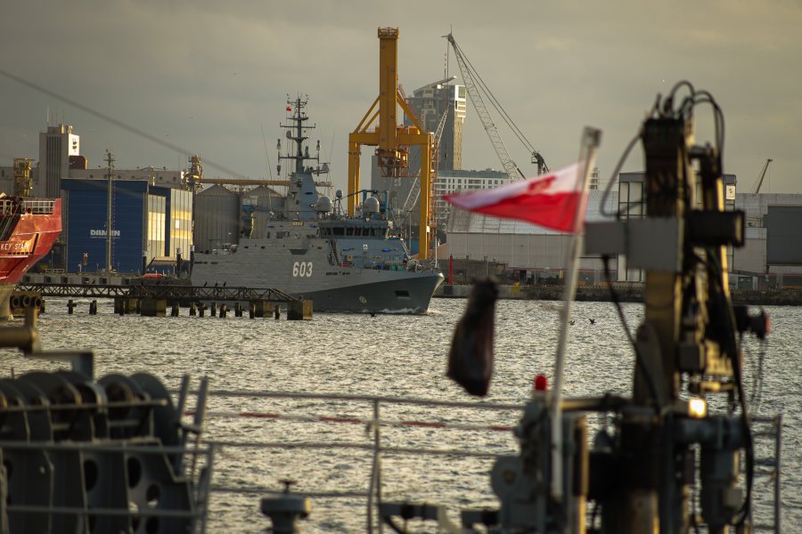 Na pierwszym planie fragment pokłady okrętu i powiewająca biało-czerwona bandera. Z tyłu niszczyciel min ORP „Mewa” wpływający do Portu Wojennego w Gdyni // fot. st. mat Ariel Szczepański/ facebook.com/Marynarka Wojenna RP