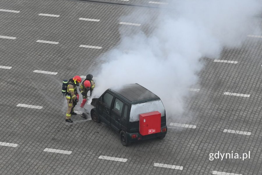 Strażacy gaszący płonący samochód osobowy stojący na pustym parkingu
