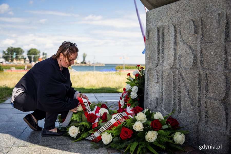Kobieta składa kwiaty pod pomnikiem.