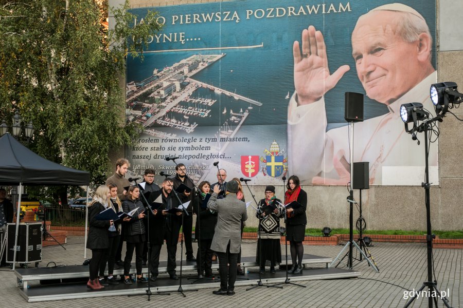Występ chóru z okazji obchodów Dnia Papieskiego w Gdyni. Artyści stoją przy bazylice mniejszej w Gdyni na tle baneru z Janem Pawłem II // fot. Karol Stańczak