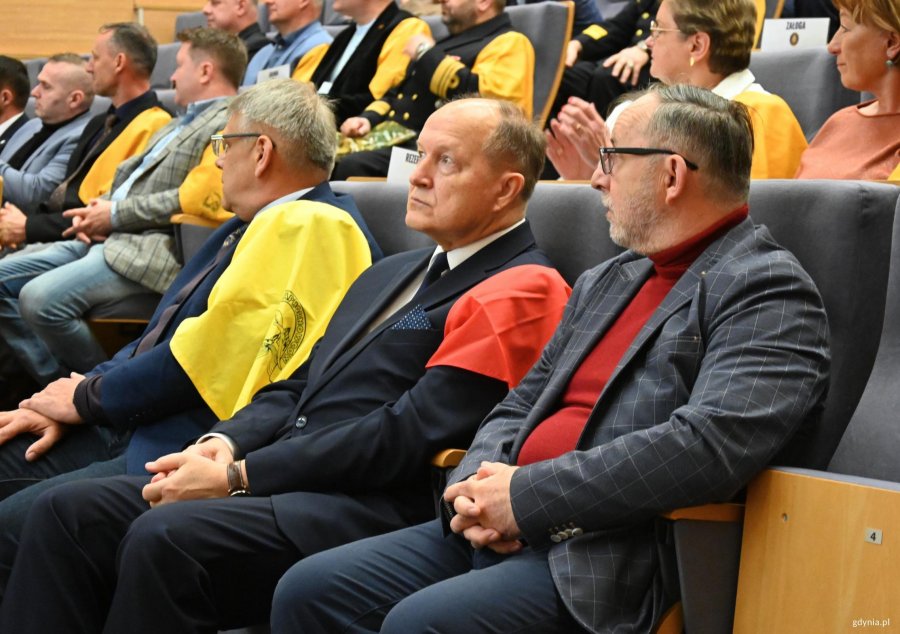 Mężczyźni w garniturach z chustami na ramionach, tylko jeden ma czerwoną