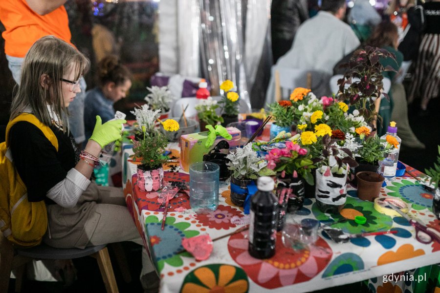 Warsztaty ekologiczne w strefie Kids Zone. Dziewczynka tworzy doniczkę z plastikowej butelki. Na stole stoją butelki i kwiaty // fot. Karol Stańczak