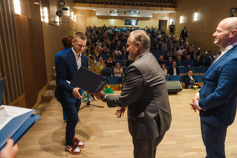 Uczeń odbierający dyplom z rąk prezydenta miasta, w tle publiczność wydarzenia