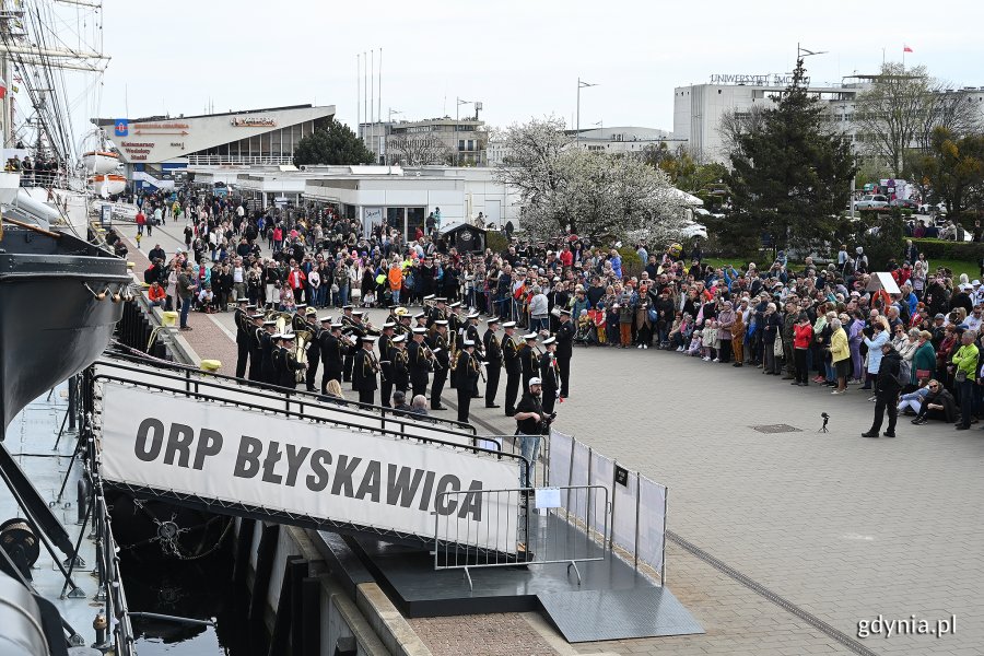 Orkiestra Marynarki Wojennej daje koncert przed okrętem ORP Błyskawica. Przed nimi stoi tłum ludzi, uczestników majówki.