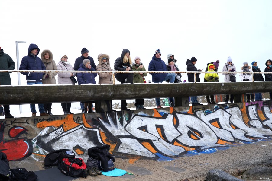 Grupa ciepło ubranych ludzi obserwuje plażę
